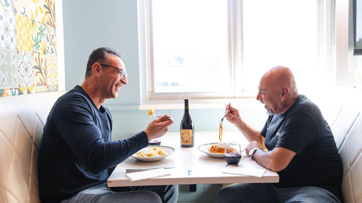 Two men enjoying pasta dishes and a bottle of red wine at Jay Luigi restaurant in St. Pete.