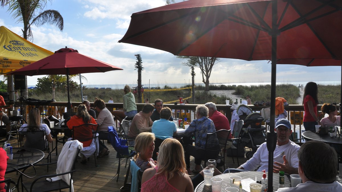 A large group of people at the outdoor area of a beachfront restaurant.