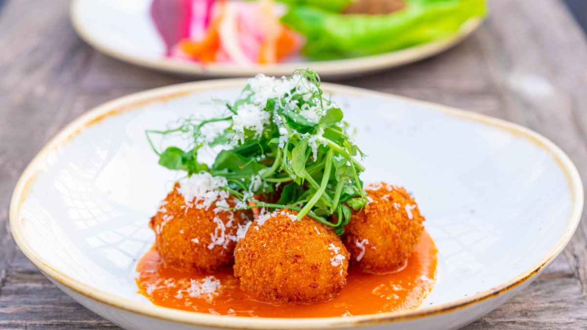 Image of food dish at Two Graces restaurant in St. Pete. Featuring a bowl with fried balls in a red sauce and greens on top.
