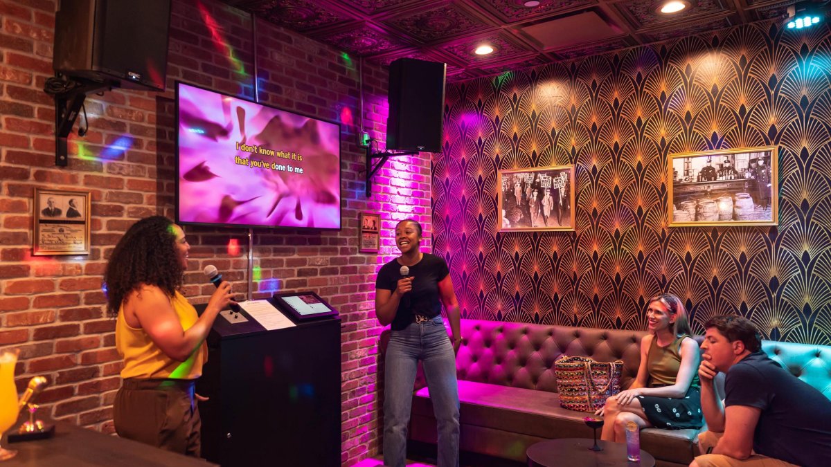 two black women smile while singing karaoke at LALA in St. Pete while two friends watch while seated