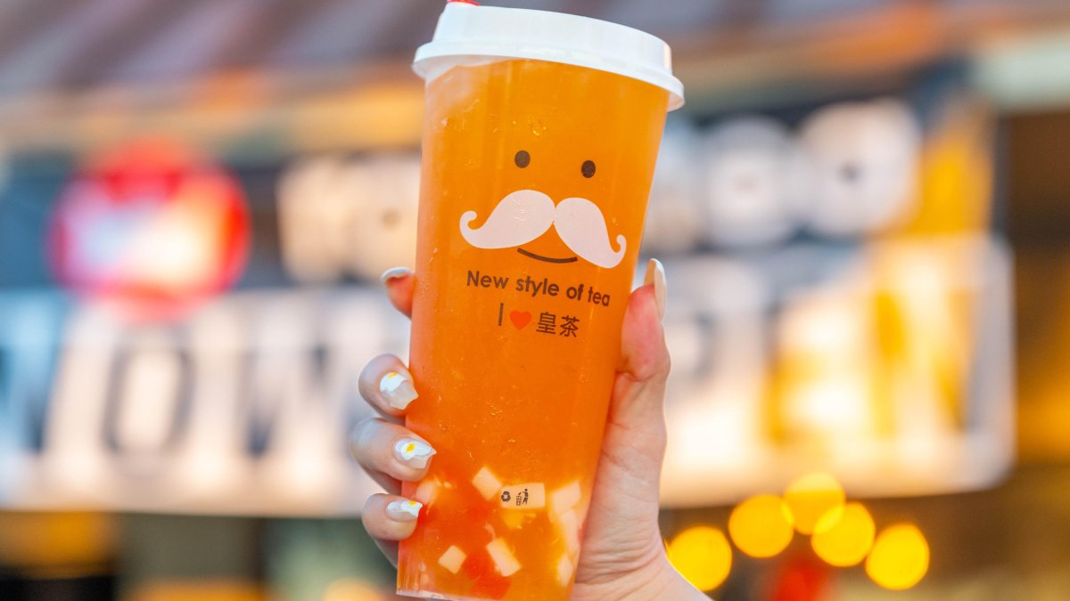 a young woman with a French manicure holds up a cup of iced tea from RoyalTea in Pinellas Park, the cup has a face with a mustache on it