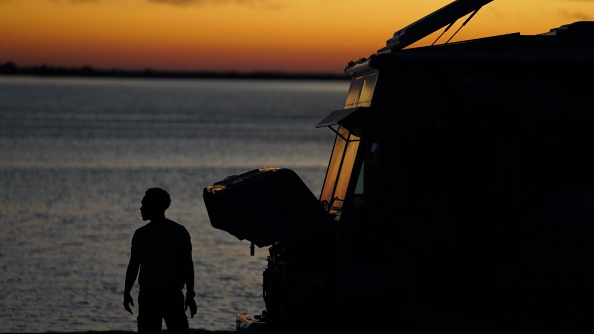 Man standing outside watching the beach during evening sunset. Featuring yellow sunset skies and a food truck.