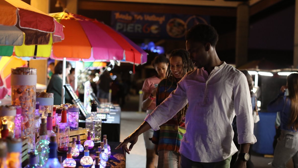 Three people looking at colorful shopping booths and pointing out items they like at Pier 60 in Clearwater Beach.