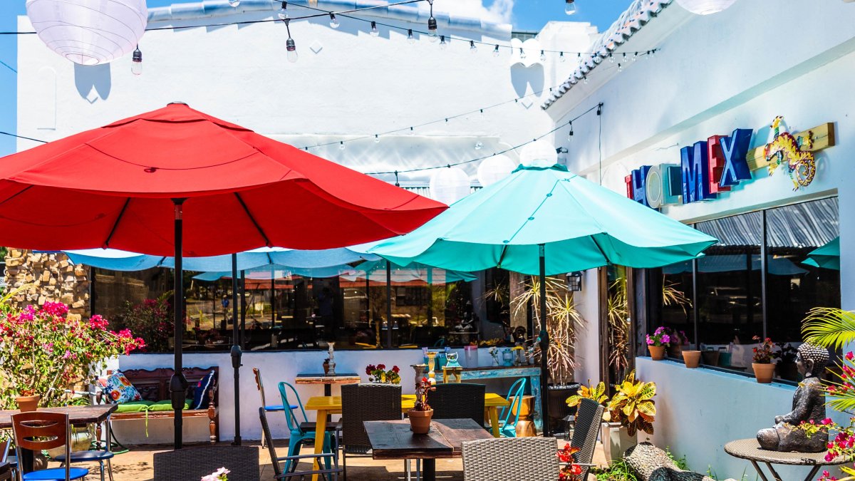 Outside photo of the patio seating area at Nitally's ThaiMex restaurant. Featuring red and blue umbrellas, white string lights and lots of outdoor plants.