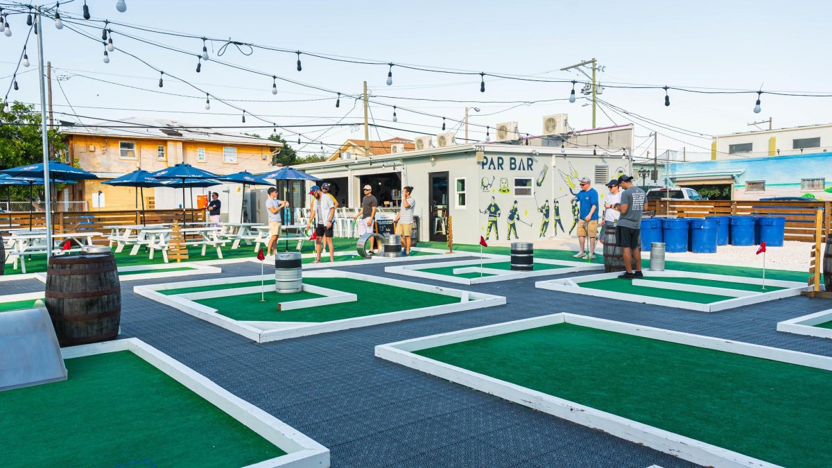 Outside image of mini-golf bar Par Bar, featuring various holes, string lights and giant beer pong.