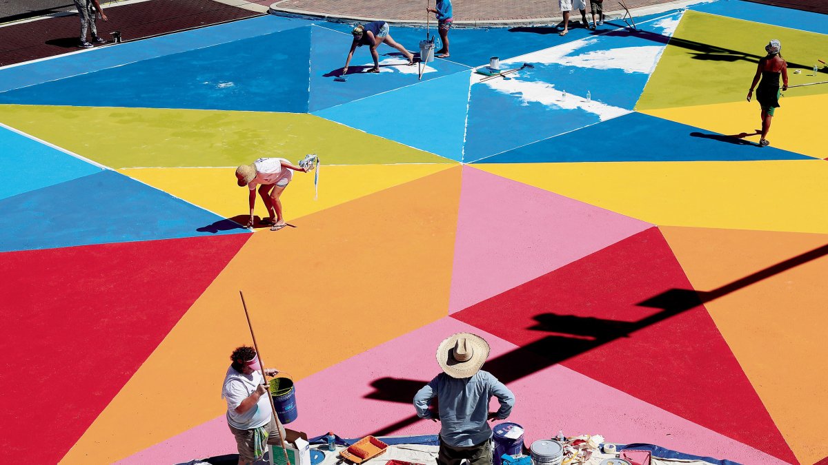 several people painting a brighly colored geometric mural called "Common Ground" on the pavement of Central Ave. in St. Pete