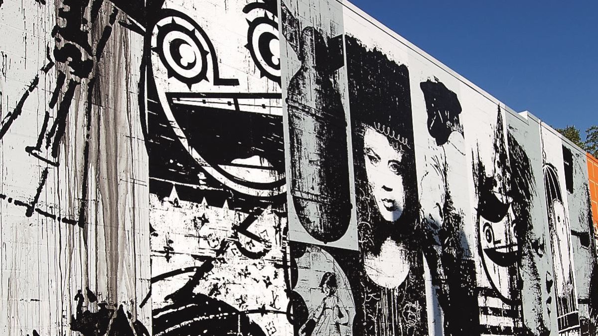 a graphic mural in black and white of many faces is on the side of a building with clear blue sky above