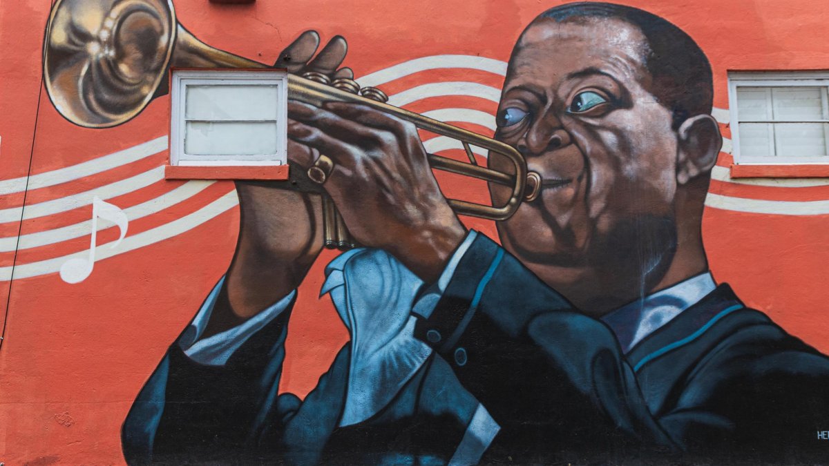 A mural by Herbert Davis in South St. Pete on a red background depicts Louis Armstrong playing the trumpet