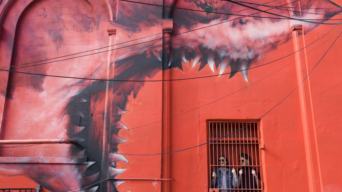 two people "hide" behind an iron door next to an enormous red mural of a great white shark