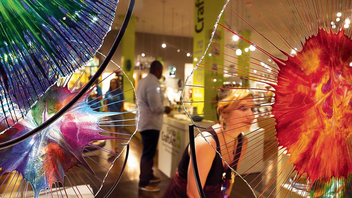 una mujer con un vestido negro observa una hermosa obra de arte en vidrio naranja y transparente en la galería Florida CraftArt en St. Pete