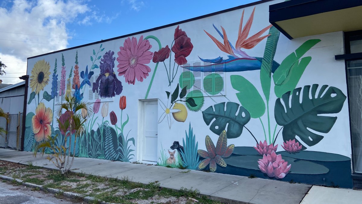 Large flower street mural with white background featuring Florida-inspired green palms, colorful spring flowers, tulips and two dogs.