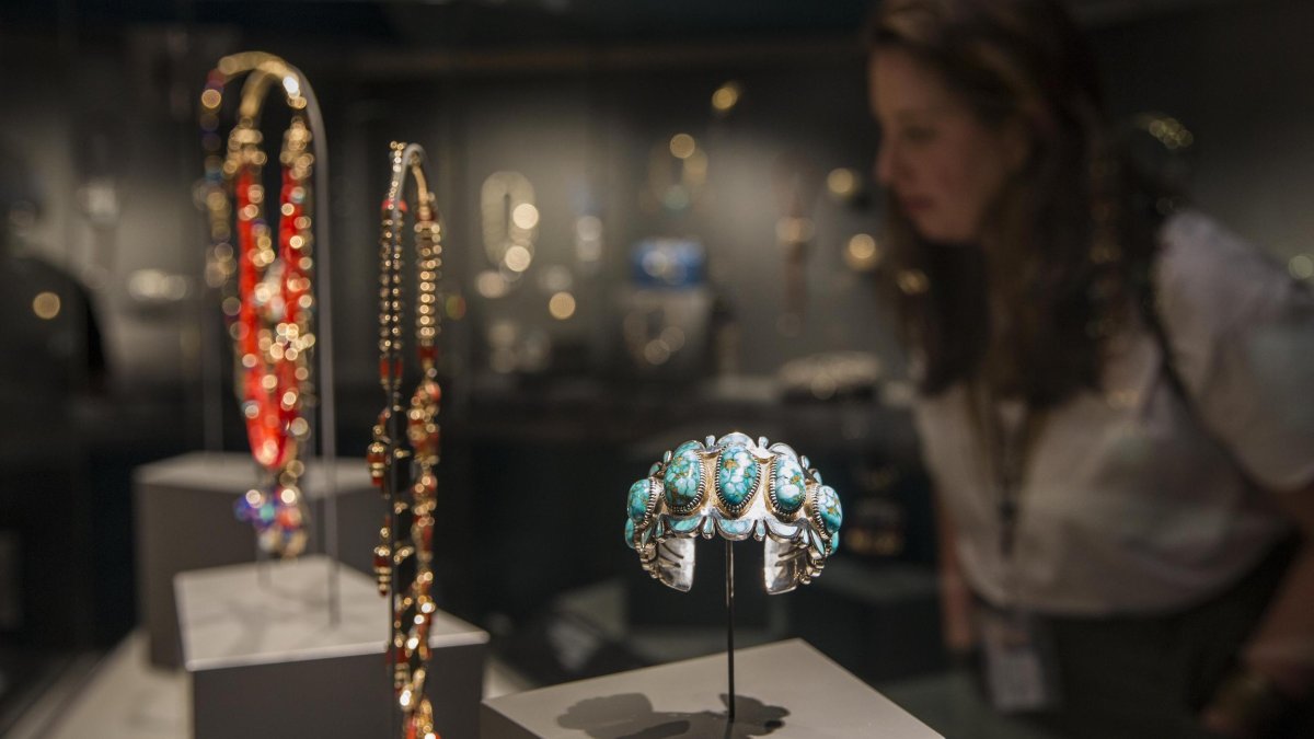 a woman looks at a glass case of Native American jewelry including a turquoise bracelet at the James Museum