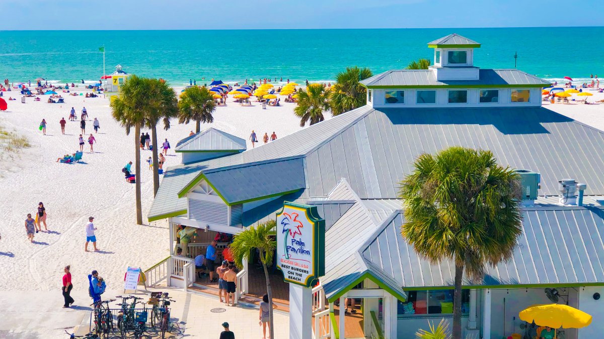 Outside of the Palm Pavilion restaurant on Clearwater beach with people walking around outside featuring blue ocean water.