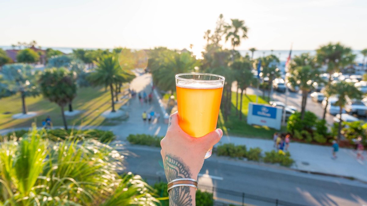 A hand holding a cold pint of craft beer from the balcony of 3 Daughters Brewing in Clearwater Beach on a sunny afternoon.