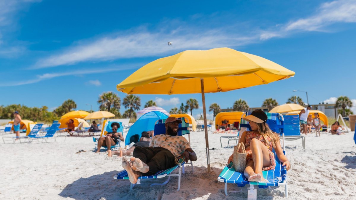 a couple relaxes on lounge chairs under a bright yellow umbrella on the white sands of Madeira Beach