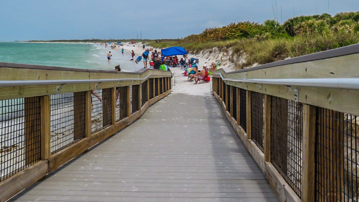 boardwalk leading to white sand beach lined with dunes with beautiful green water at Fort De Soto