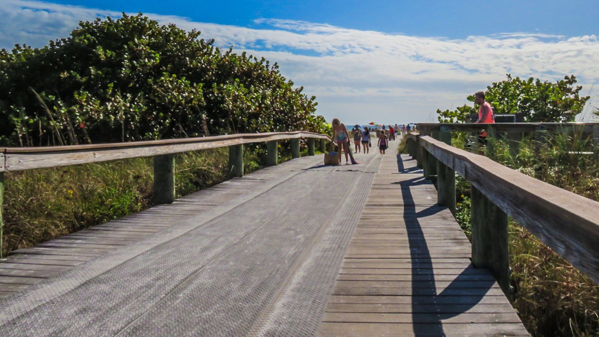 a wooden walkway with a mat surface runs to the sand, with vegetation on either side at Upham Beach