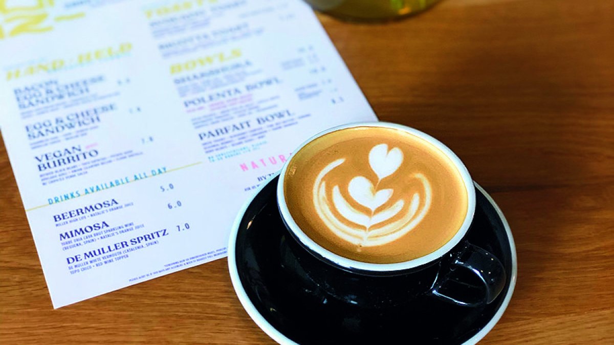 a cup of cappuccino with a pretty foam design in a black cup and saucer next to the menu for Bandit Coffee in St. Pete