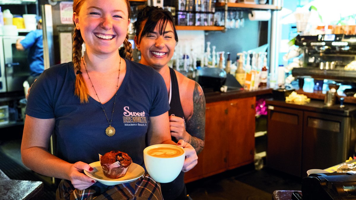 Two young female workers hold coffee and muffin in wood-accented coffeehouse