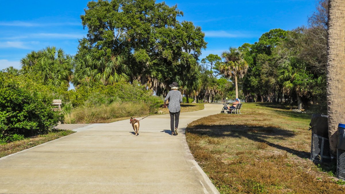 Paved trail with woman walking dog at Clam Bayou Nature Preserve.