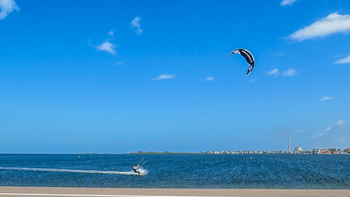 A kite surfer flies across flat, blue water at Fred Howard Park.
