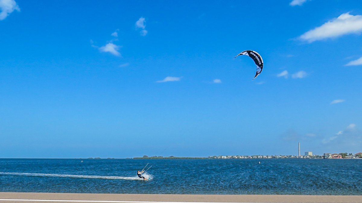 A kite surfer flies across flat, blue water at Fred Howard Park.