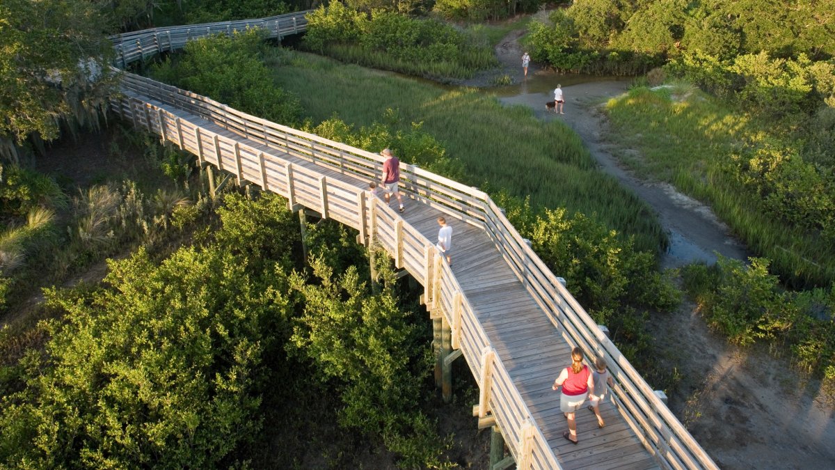 A wooden boardwalk with a few people walking through Boca Ciega Millennium Park