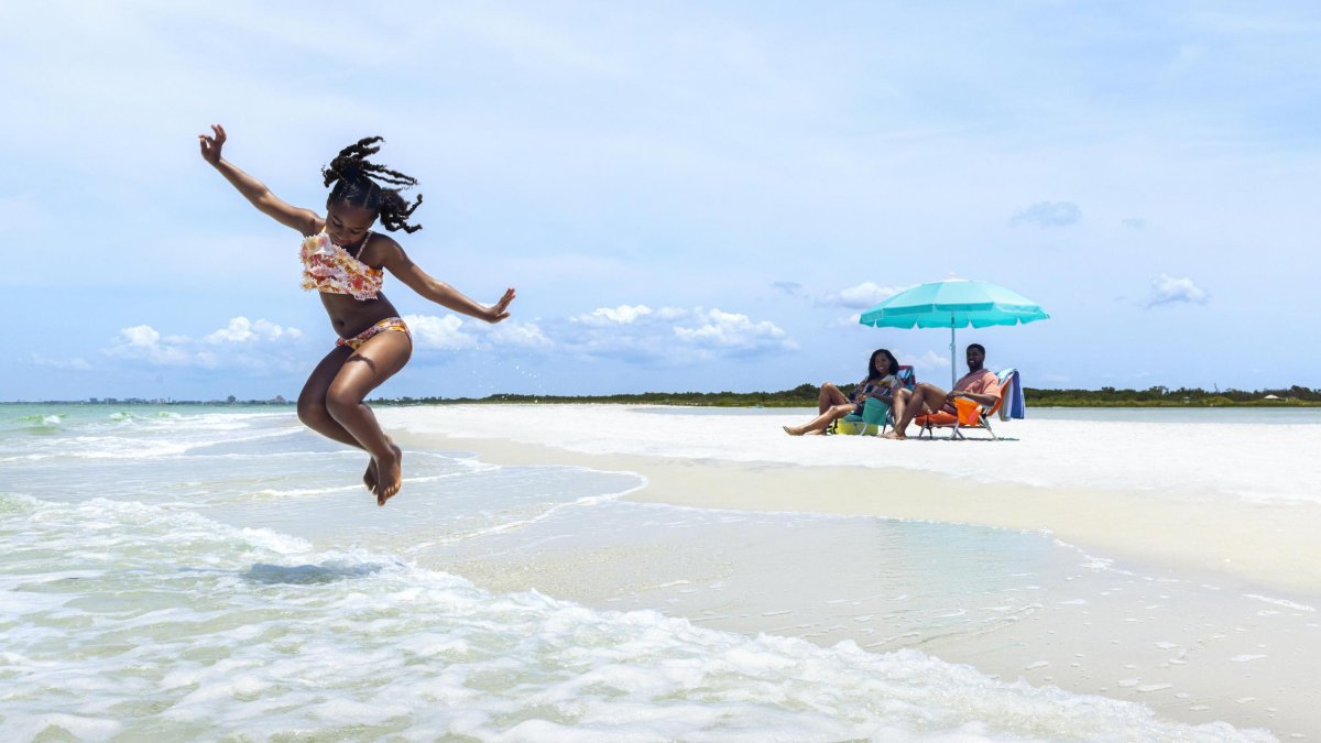 Girl jumping in water as parents watch from the beach in Fort De Soto Park.