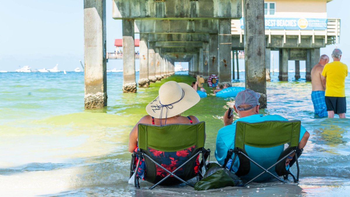 a woman and a man sit in low beach chairs in the shallow water underneath Pier 60 in Clearwater Beach