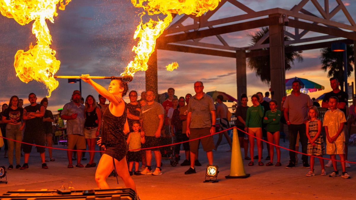 a woman in black shorts and tank top juggles with fire while spectators watch at Pier 60 in Clearwater Beach