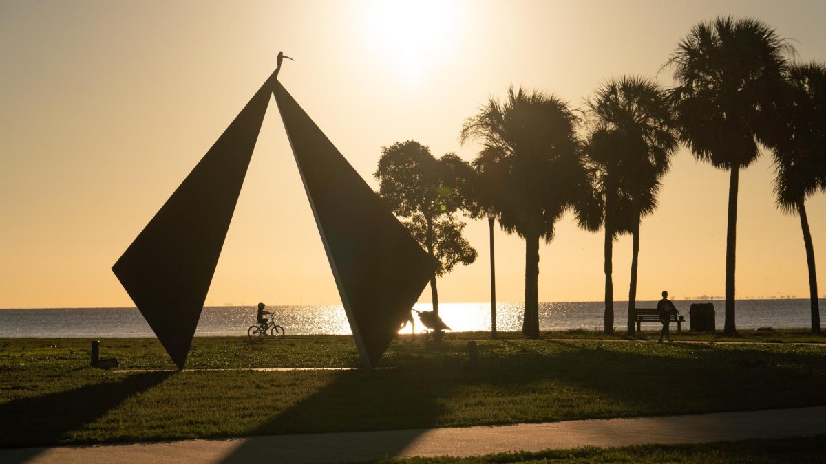 The Truth Sculpture and people walking in Vinoy Park are silhouetted by the sun.