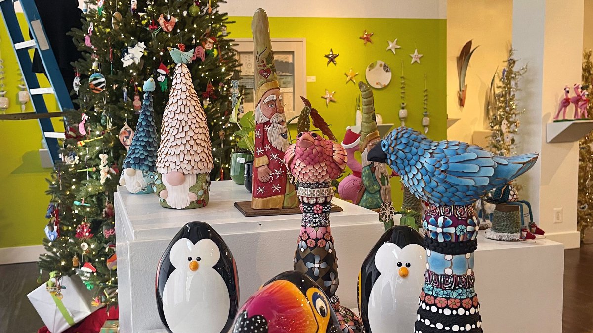 Woman standing on a ladder in Florida CraftArt store featuring a Christmas Tree and other holiday decor.