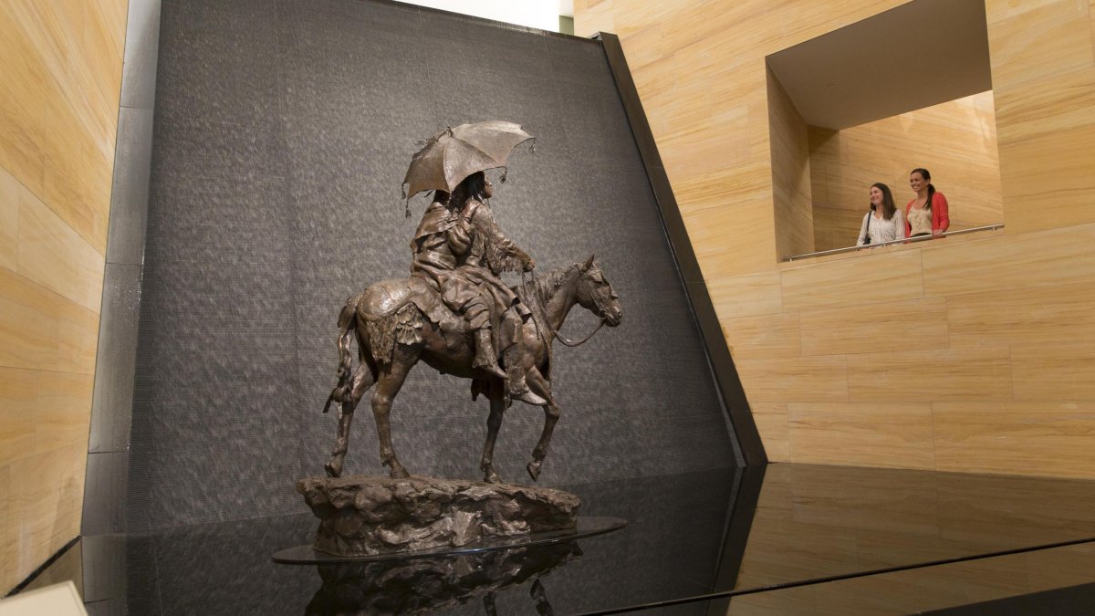 Two people peer at the waterfall and sculpture in the James Museum lobby.