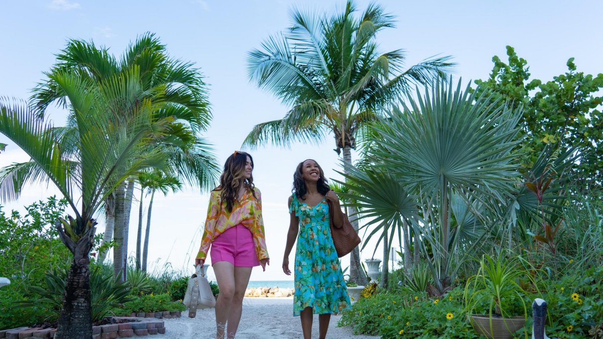 two women in colorful summer clothes walk down a path lined with palm trees away from St. Pete Beach