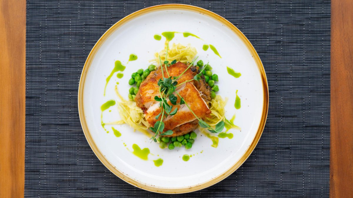 a beautiful plate of fish surrounded by garland and delicate sauces on a teak wood table