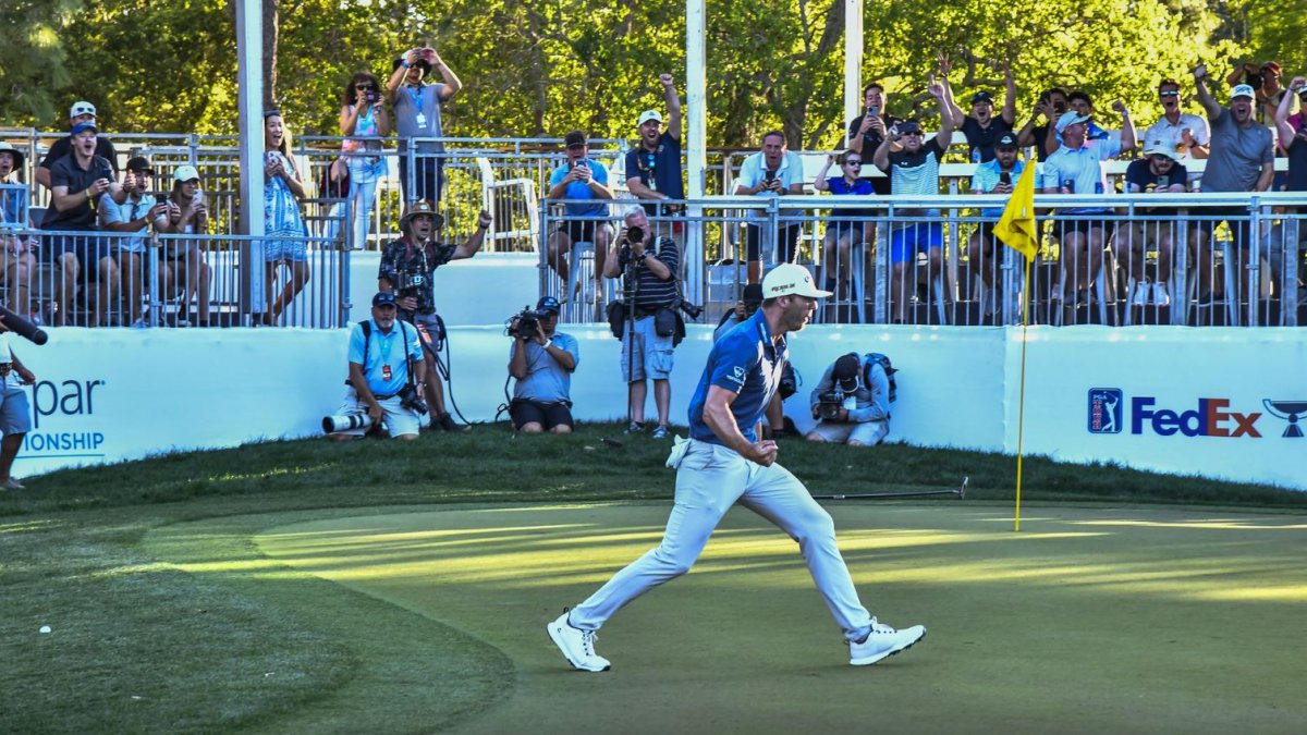 Male golfer walking on a golf course in front of a crowd of people.