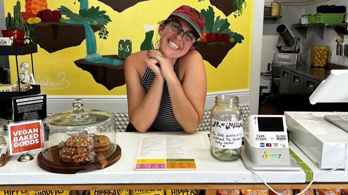 A woman behind a store counter with chips in front and a yellow mural behind