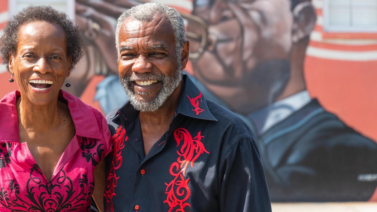 Black man and woman in front of mural of Louis Armstrong
