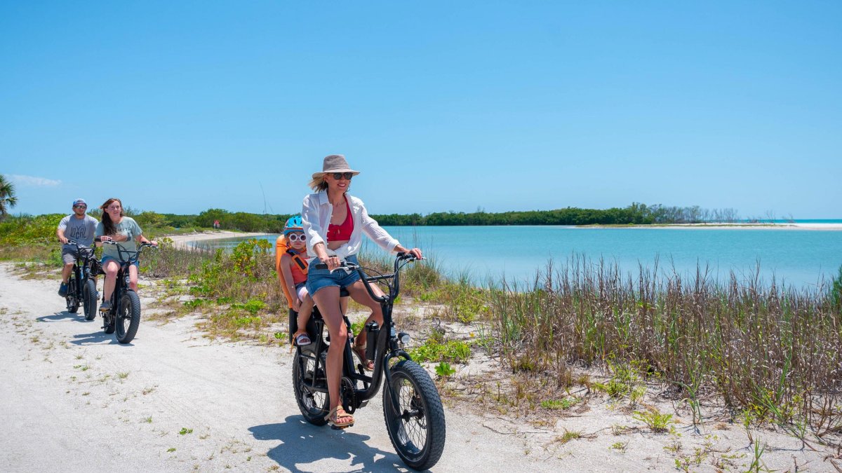 Familie fährt mit E-Bikes auf einem Sandweg am Wasser entlang