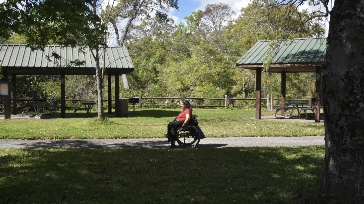 Woman in wheelchair rolls along paved path through park