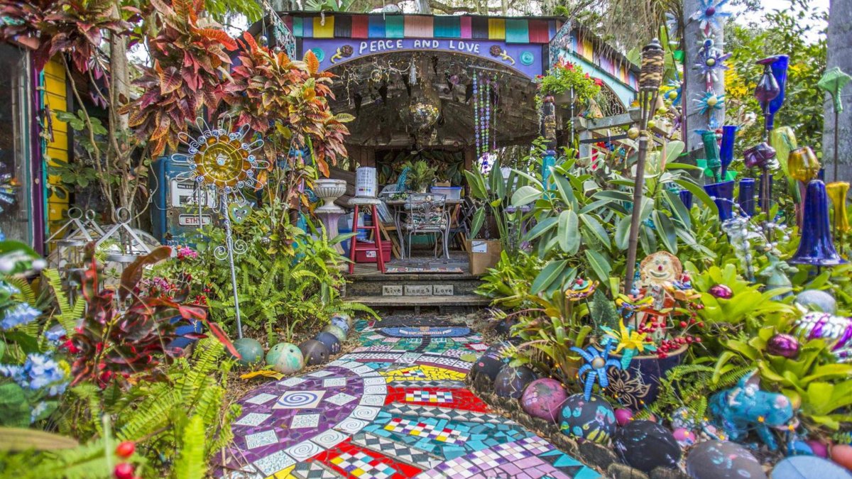 Bunte Mosaikfliesen führen zu einem „Peace and Love“-Baldachin im Garten von Whimzeyland in Safety Harbor, Florida