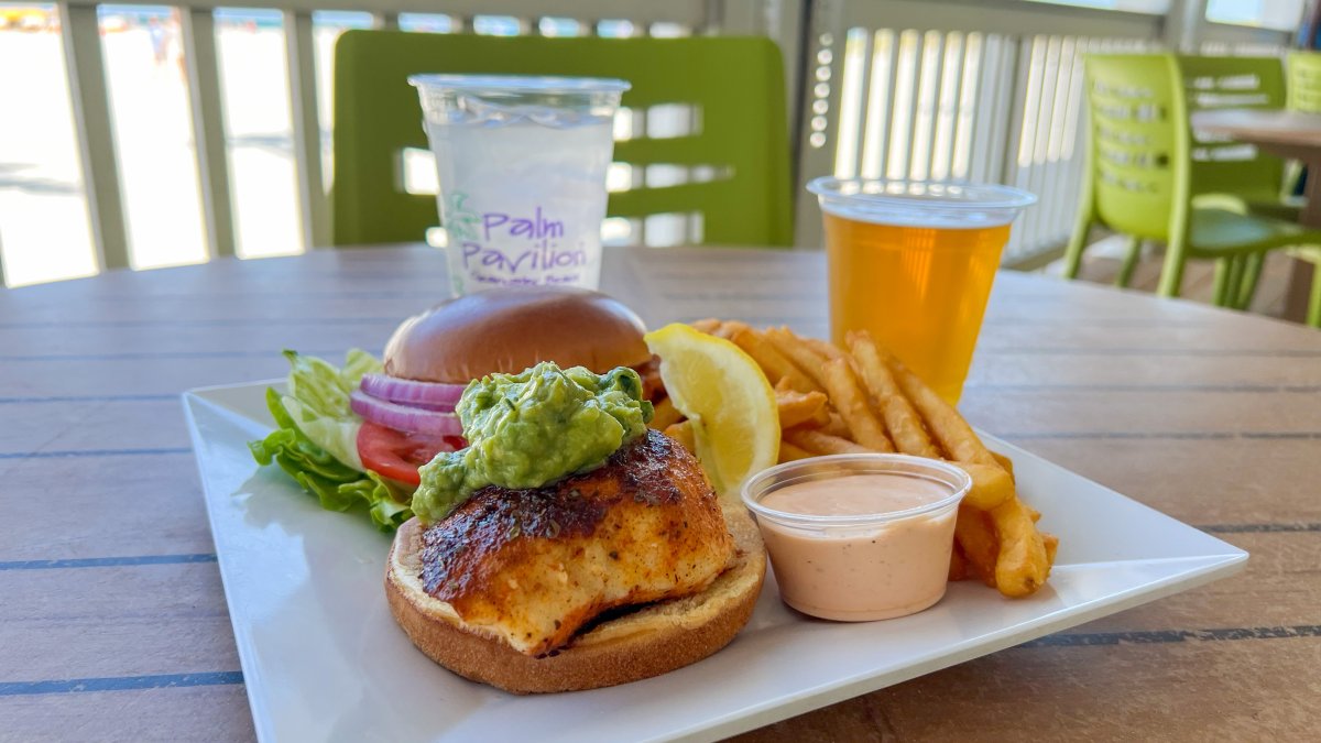 a blackened grouper sandwich with guacamole on top on a brioche bun with fries and a beer at Palm Pavilion in Clearwater Beach