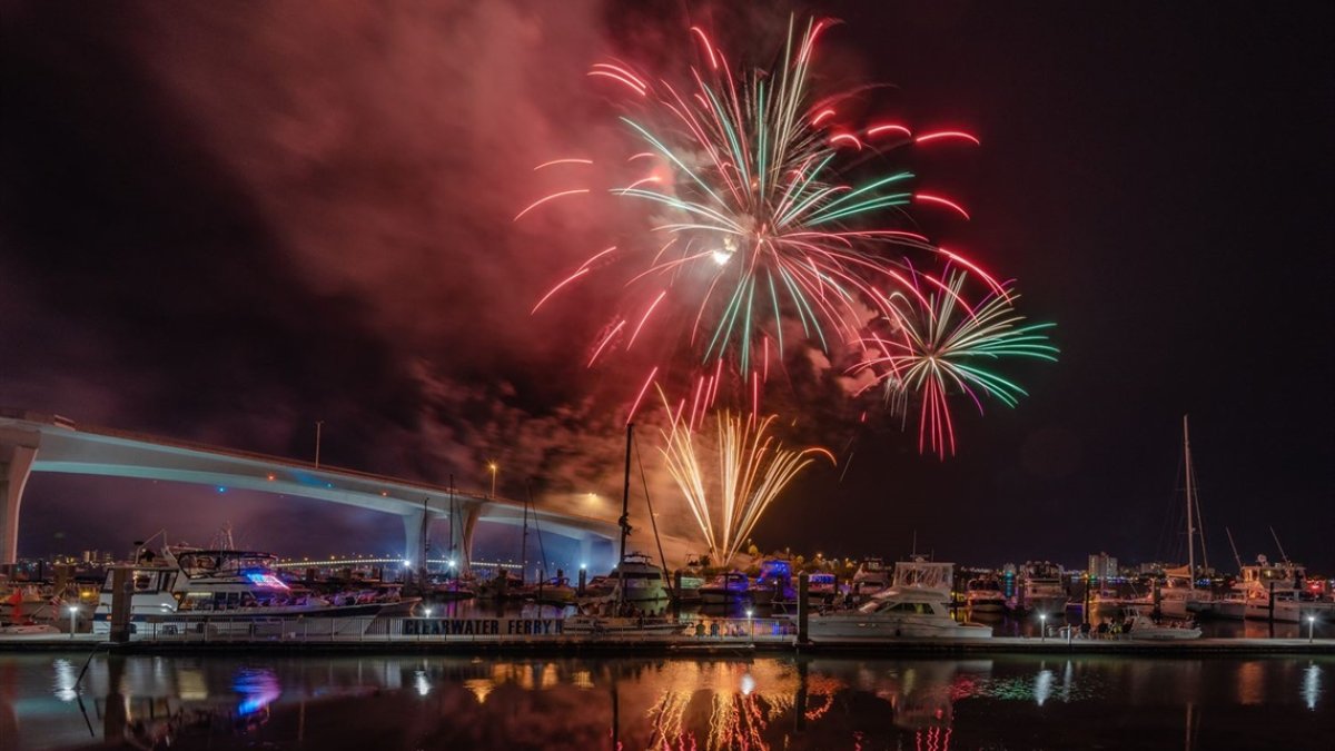 Red and green fireworks exploding in the night sky in Clearwater, FL over a bay of water.