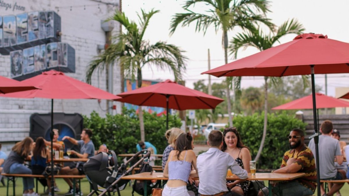 People sit at picnic tables under red umbrellas in a beer garden