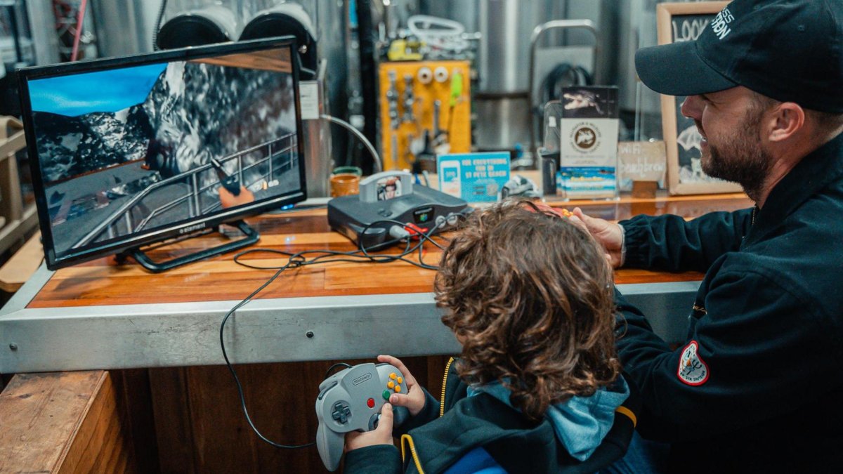 A man and boy play an old-style videogame inside a brewery.