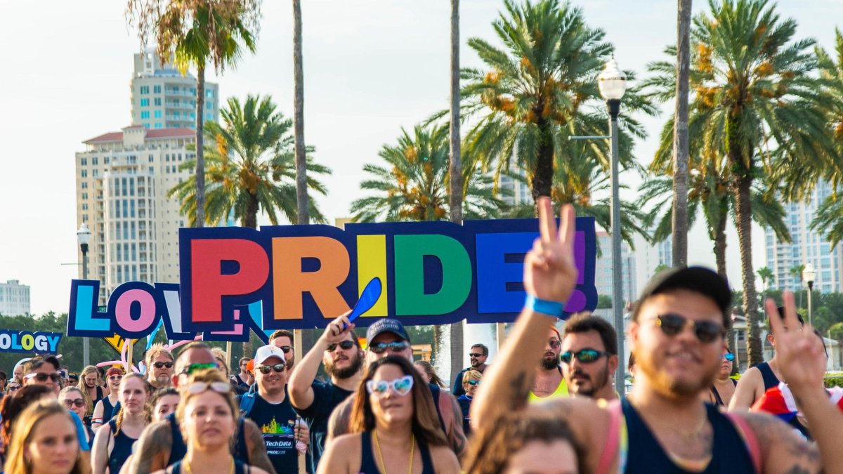 A large group holding up colorful Pride signage during the Saint Pete Pride parade celebration in Saint Pete, Florida.