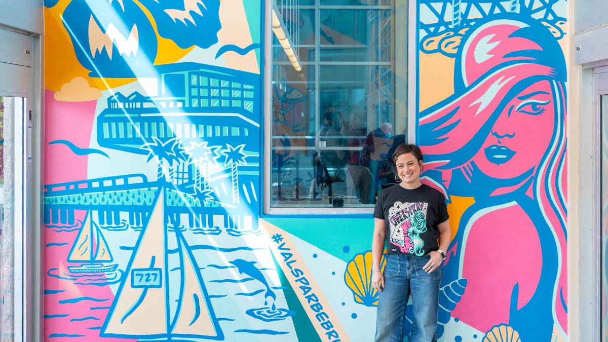 a person in jeans and a black t-shirt stands in front of a pastel colored mural named "be bright" at St. Petersburg Clearwater International Airport