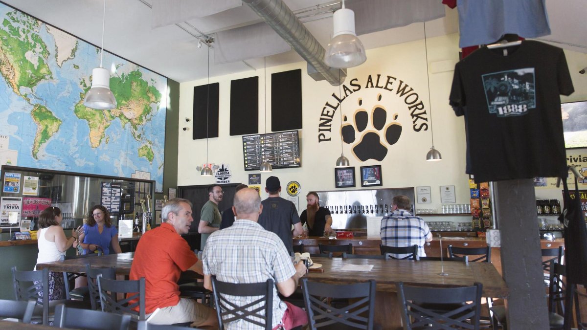 People drink beer at tables at Pinellas Ale Works with PAW logo on wall