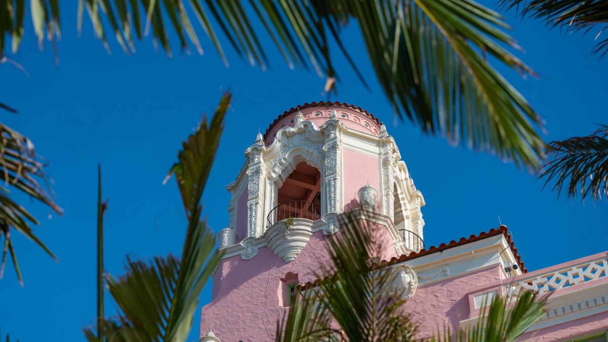 palm trees frame a view of the pink and white tower at the Vinoy Hotel in St. Pete under a clear blue sky