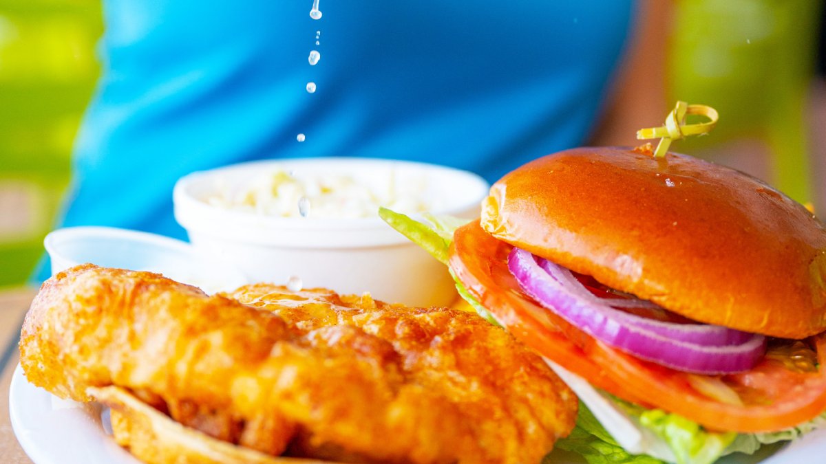 a person squeezing lemon on a fried fish next to a sandwich with tomato, lettuce and onion.